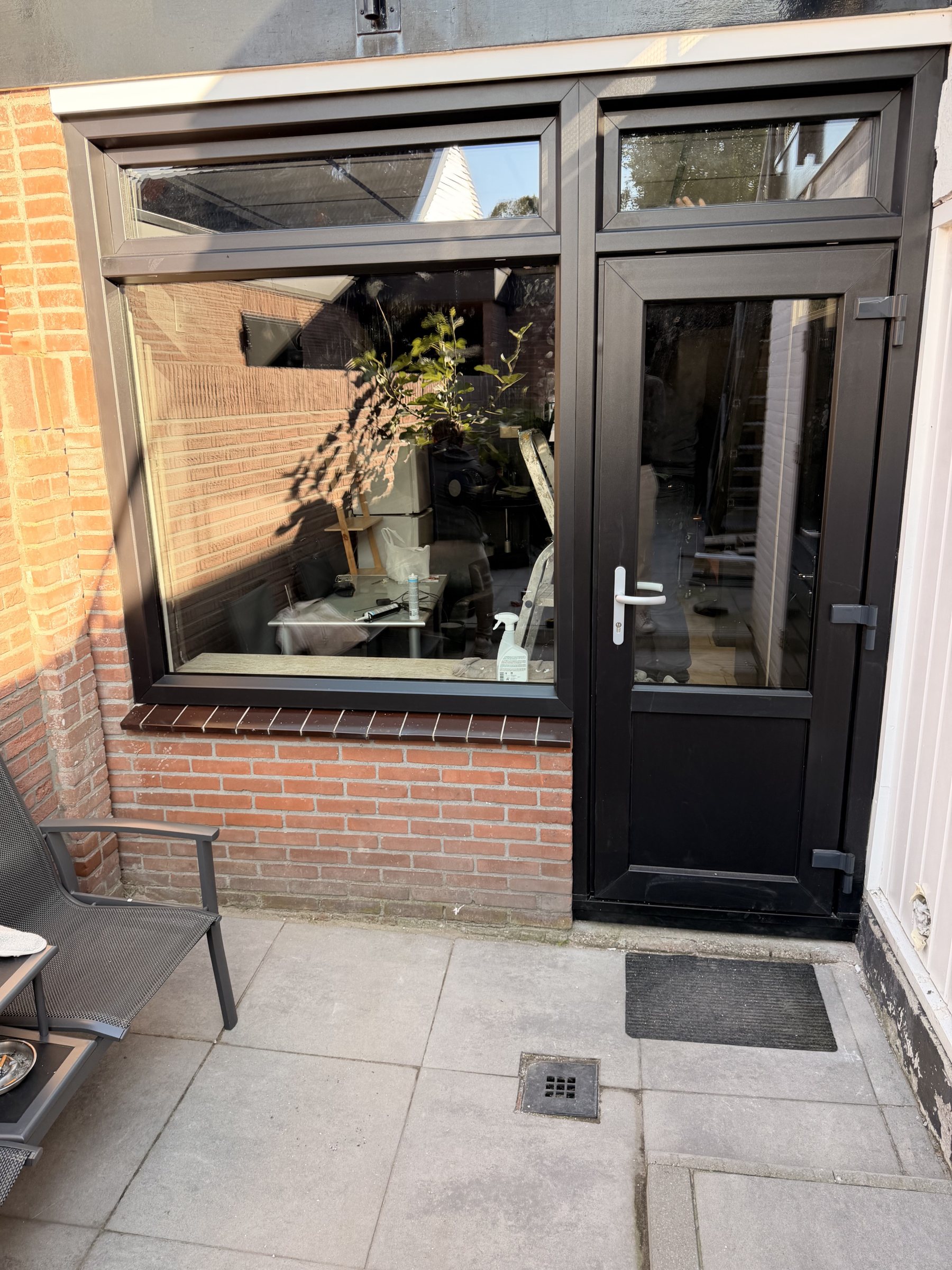 Donkere kunststof achterdeur met glas, een onderpaneel en een passend raam ernaast